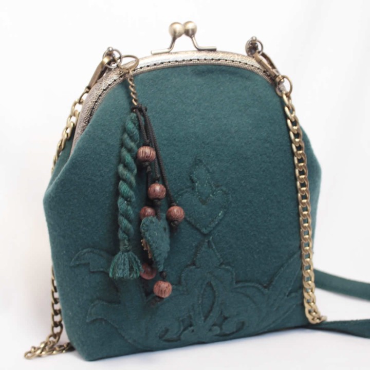 Borsa con cerniera, ricami decorativi e ciondolo.